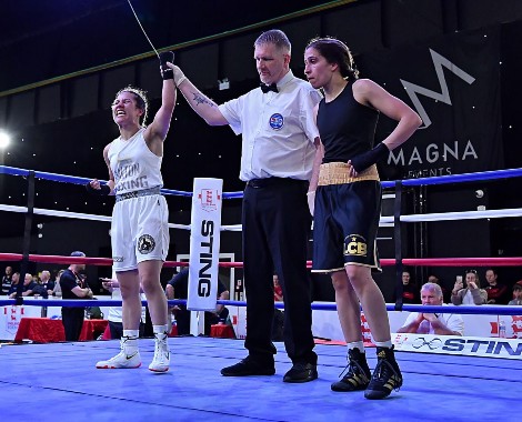 A boxing referee raises Rhea Kanu's left arm aloft in the centre of a boxing ring.